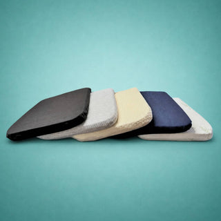 Stack of 100% organic latex seat cushion with organic cotton, denim, and bamboo covers in various colors on a light blue background